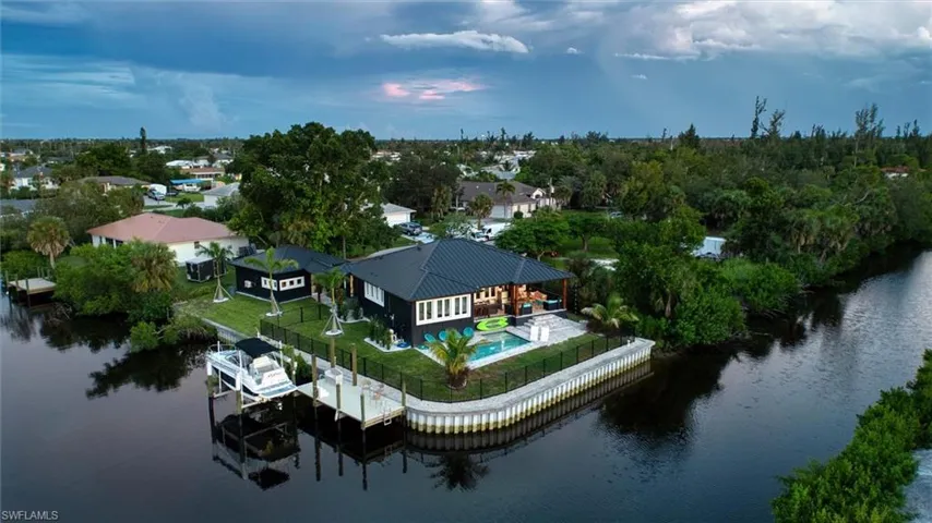 Waterfront property featuring a black exterior, a dark metal roof, an inground pool with a surrounding patio, a private dock with a boat lift, and a canal-front bulkhead
