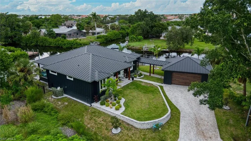 Waterfront property featuring a dark-toned exterior with a metal roof, an attached covered walkway, a paver driveway, and a detached garage with a wood-finish door