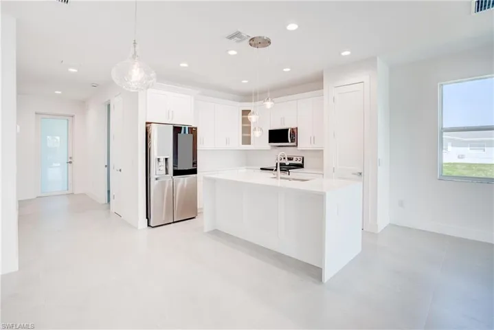 Kitchen with stainless steel fridge, light countertops, glass insert cabinets, white cabinets, and recessed lighting
