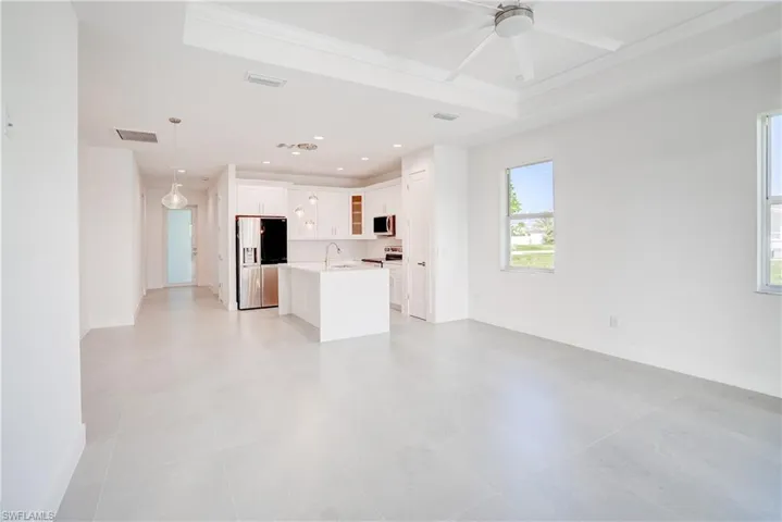 Unfurnished living room with ceiling fan, ornamental molding, a raised ceiling, and recessed lighting