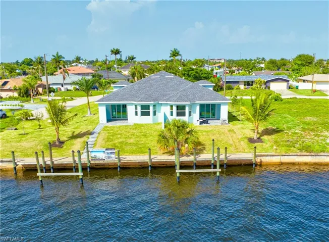 Rear view of property featuring a water view, roof with shingles, a lawn, stucco siding, and a residential view