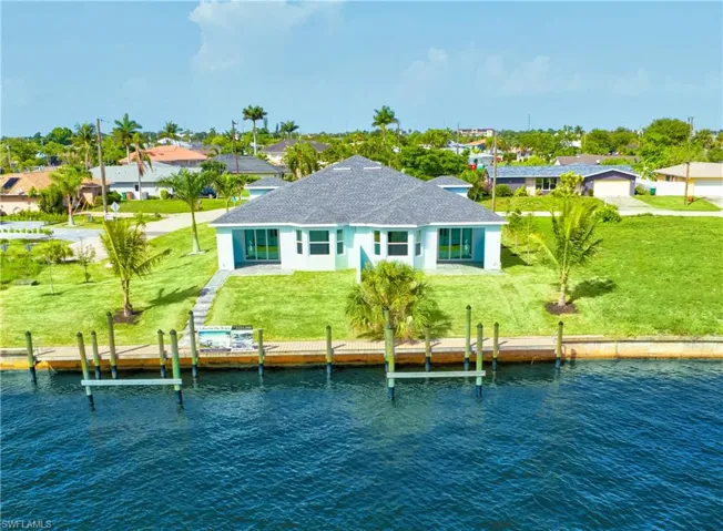 Rear view of house with a water view, a shingled roof, a residential view, and a lawn