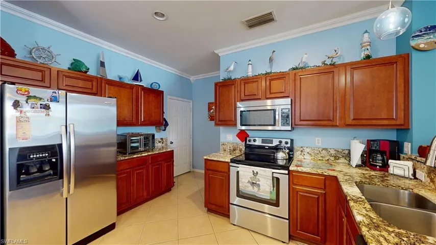 Kitchen featuring appliances with stainless steel finishes, decorative light fixtures, light stone countertops, light tile patterned flooring, and ornamental molding