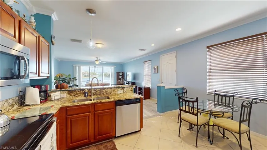 Kitchen featuring light tile patterned flooring, light stone counters, ceiling fan, stainless steel appliances, and sink