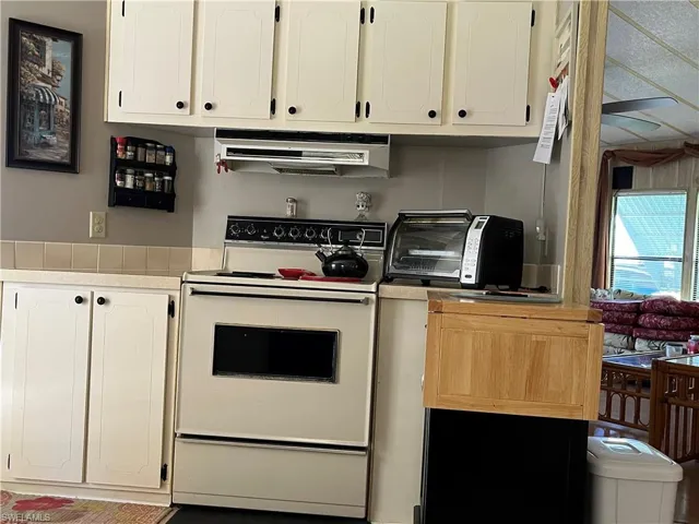 Kitchen featuring white cabinetry, ventilation hood, and white stove