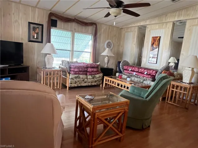 Living room featuring wood walls, ceiling fan, lofted ceiling, and wood-type flooring