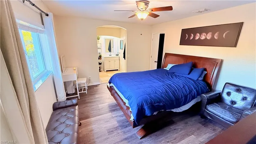 Bedroom with arched walkways, wood finished floors, ensuite bathroom, and a ceiling fan