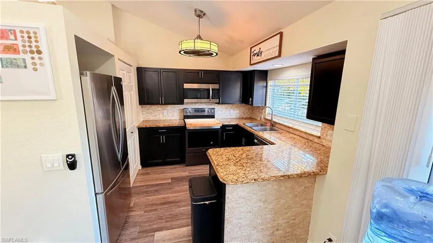 Kitchen with stainless steel appliances, light stone counters, vaulted ceiling, hanging light fixtures, and dark wood finished floors
