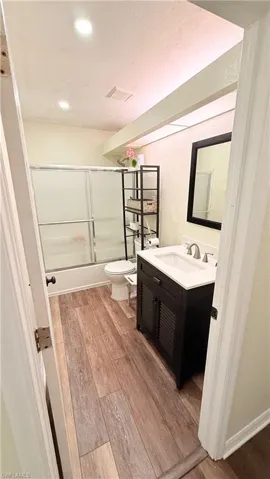 Full bathroom featuring light wood finished floors, vanity, shower / bath combination with glass door, a textured ceiling, and recessed lighting