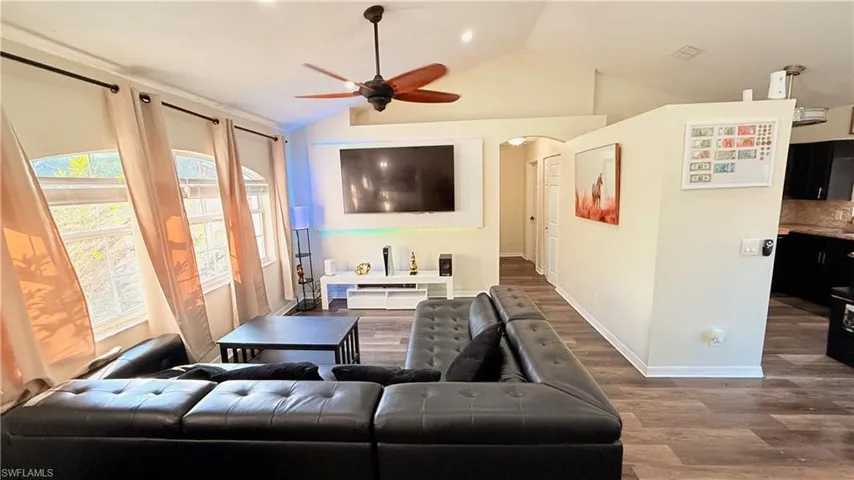 Living area with a ceiling fan, vaulted ceiling, arched walkways, and wood finished floors