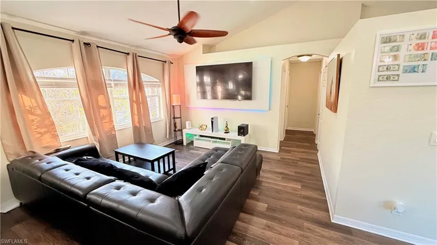 Living room featuring arched walkways, a ceiling fan, dark wood-style flooring, and lofted ceiling