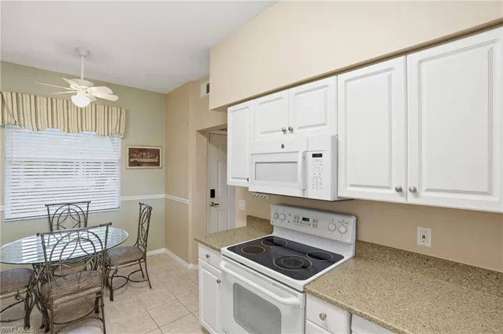 Kitchen featuring white appliances, white cabinets, a ceiling fan, light tile patterned flooring, and light stone countertops