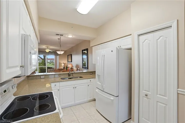 Kitchen featuring white appliances, white cabinets, light stone counters, and a peninsula