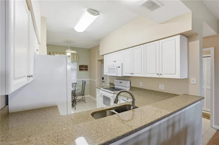 Kitchen with white appliances, white cabinets, light stone counters, ceiling fan, and light tile patterned floors