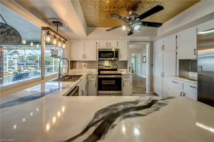 Kitchen with decorative light fixtures, stainless steel appliances, backsplash, a tray ceiling, and sink