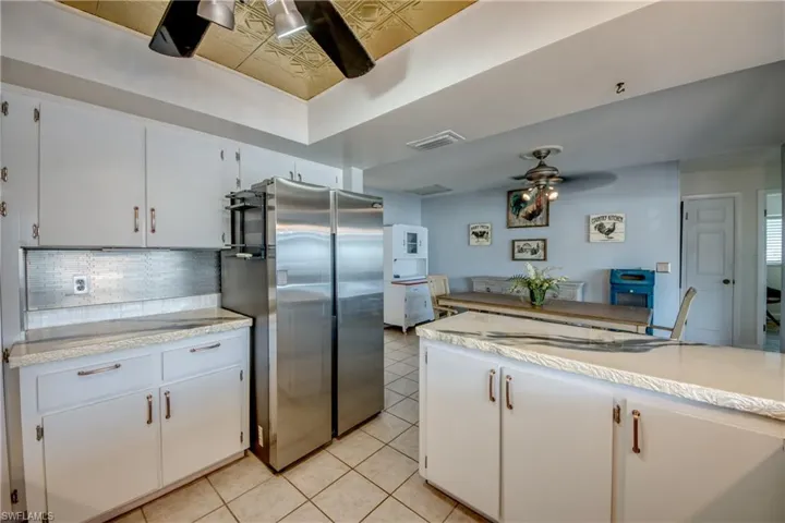 Kitchen featuring light tile flooring, backsplash, ceiling fan, stainless steel fridge, and white cabinets