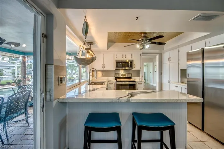 Kitchen with kitchen peninsula, stainless steel appliances, a raised ceiling, white cabinetry, and light tile floors