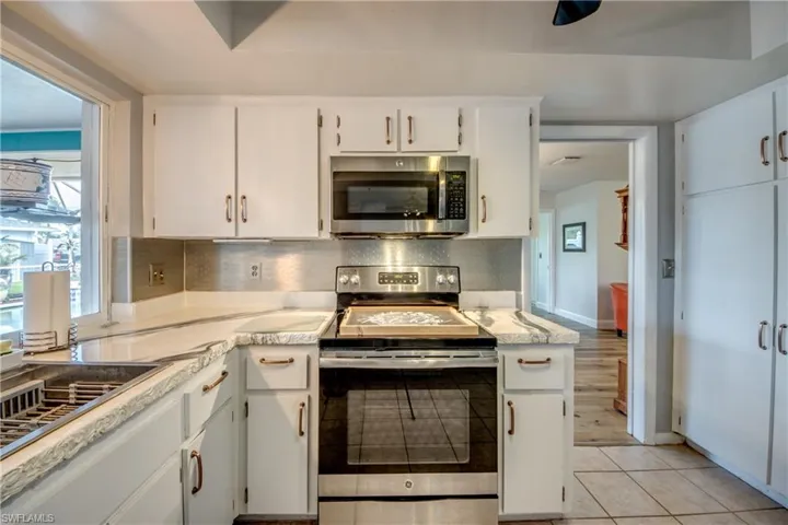 Kitchen with appliances with stainless steel finishes, white cabinetry, backsplash, and light tile floors