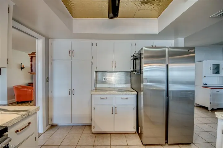 Kitchen featuring stainless steel refrigerator, light tile flooring, a tray ceiling, tasteful backsplash, and white cabinets