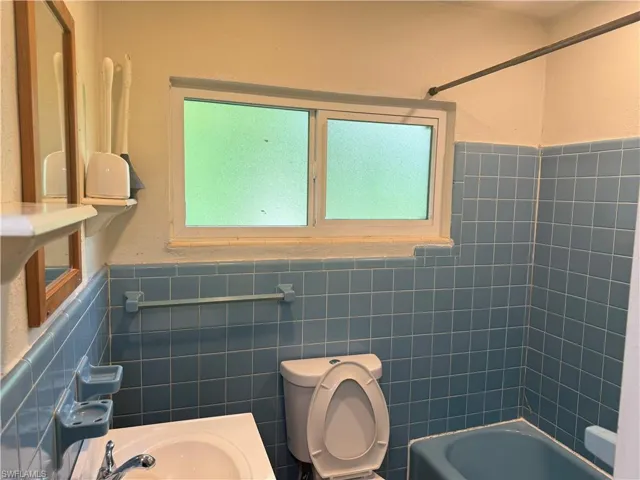 Bathroom featuring toilet, tiled shower / bath combo, and tile walls