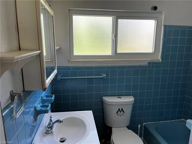 Full bathroom featuring sink, toilet, tile walls, and a wealth of natural light