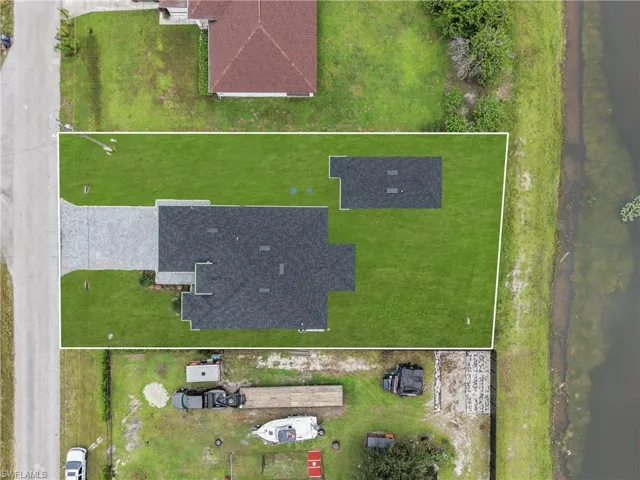 Generous lot featuring a substantial building with a dark shingle roof, expansive green lawn, and a light-colored paved driveway