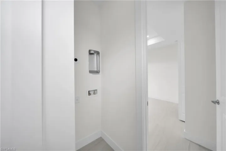 Recessed laundry hookups with white walls and light-toned flooring