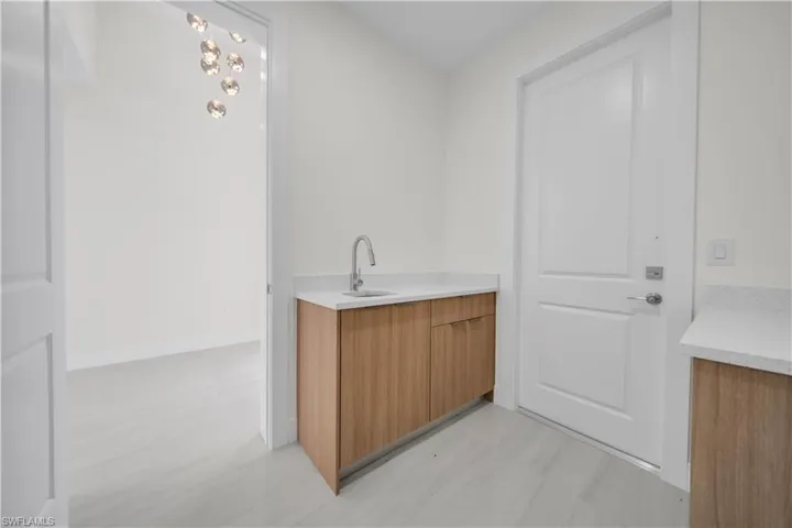 Wet bar featuring a stainless steel faucet, undermount sink, light wood-finish cabinetry, and solid surface countertop