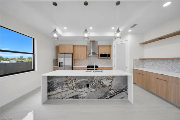 Modern kitchen featuring a waterfall island, light wood-finish cabinetry, stainless steel appliances, and a tiled backsplash