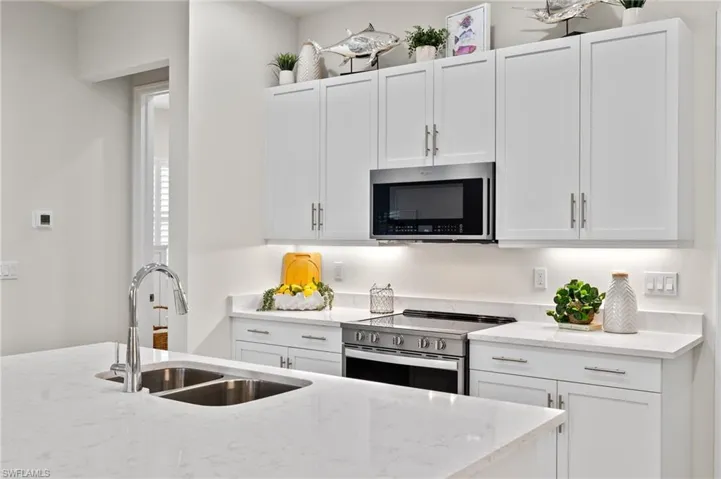 Kitchen featuring appliances with stainless steel finishes, white cabinetry, light stone countertops, and sink