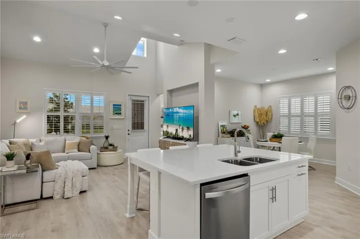 Kitchen with white cabinetry, ceiling fan, stainless steel dishwasher, sink, and a center island with sink