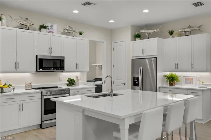 Kitchen with white cabinetry, stainless steel appliances, light wood-type flooring, an island with sink, and sink