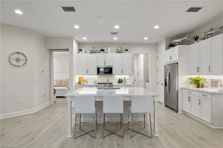 Kitchen featuring light hardwood / wood-style floors, a breakfast bar, appliances with stainless steel finishes, and an island with sink