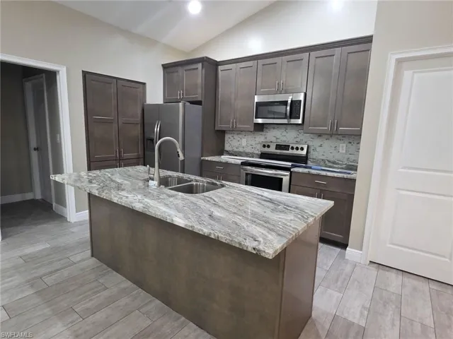 Kitchen featuring lofted ceiling, dark wood finish cabinets, stainless steel appliances, light stone counters, and wood finish floors