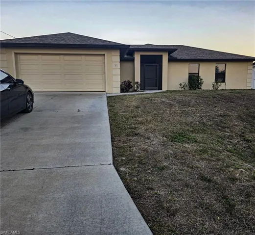 View of front facade with concrete driveway, stucco siding, roof with shingles, a garage, and a front yard