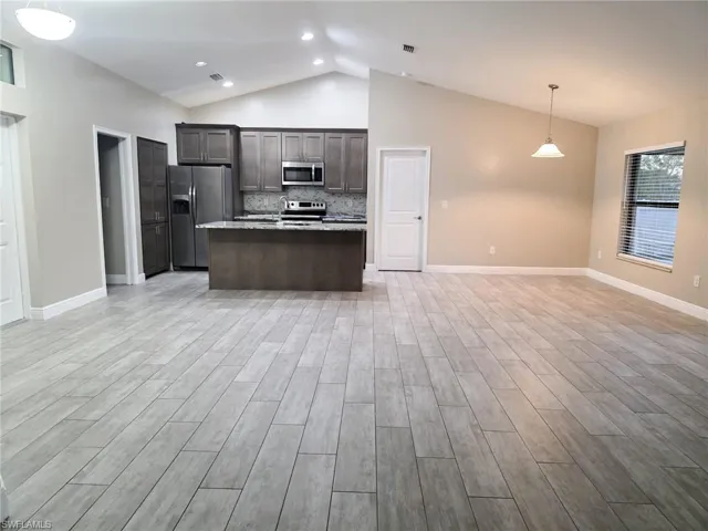 Kitchen featuring pendant lighting, dark wood finish cabinets, a center island with sink, open floor plan, and vaulted ceiling