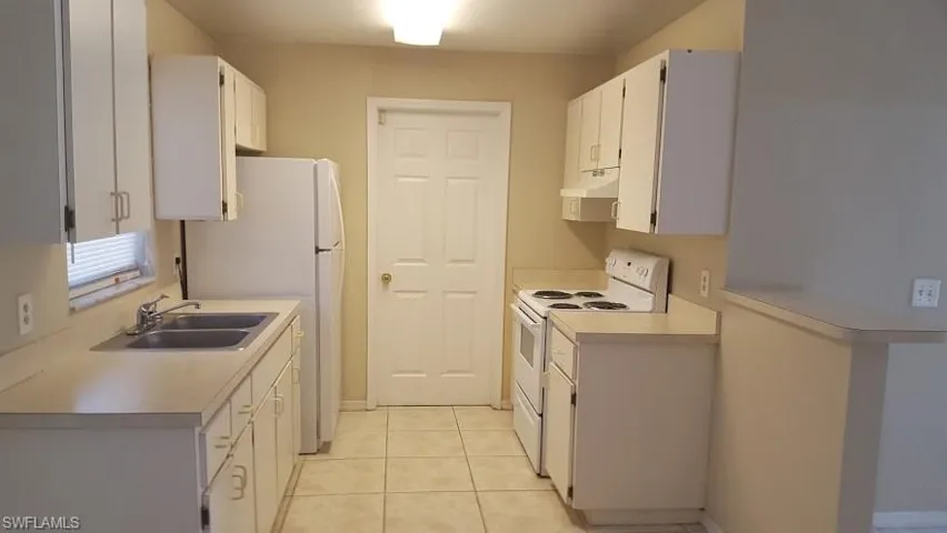 Kitchen featuring white appliances, white cabinetry, light countertops, light tile patterned floors, and under cabinet range hood