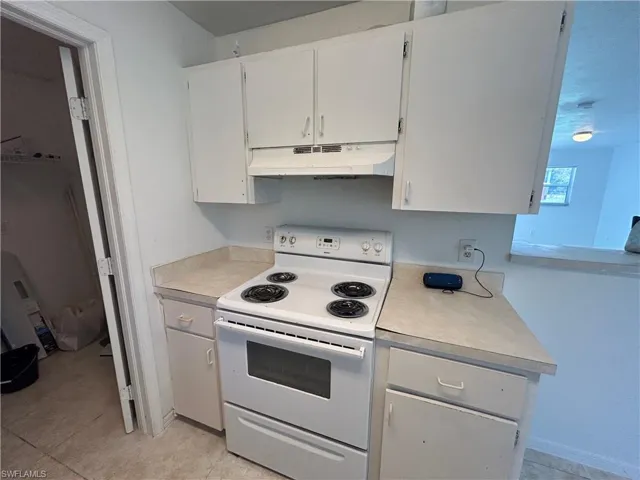 Kitchen featuring white electric range, light countertops, white cabinets, under cabinet range hood, and light tile patterned floors