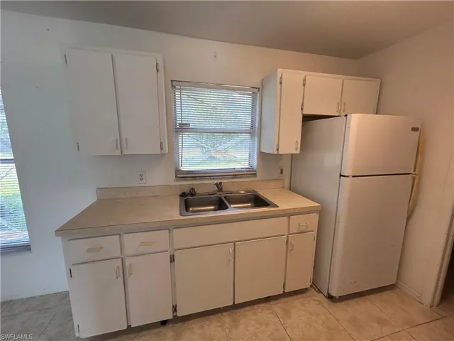 Kitchen with freestanding refrigerator, white cabinets, light countertops, and light tile patterned floors