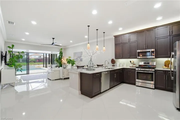 Kitchen with stainless steel appliances, dark brown cabinets, a peninsula, light stone counters, and ornamental molding