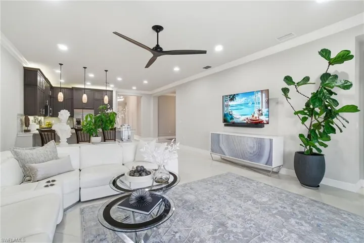 Elegant open-concept living space with crown molding, recessed lighting, modern ceiling fan, and light tile flooring, ideal for relaxed living and entertaining.
