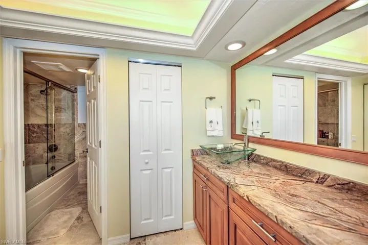 Bathroom featuring a raised ceiling, vanity, and combined bath / shower with glass door
