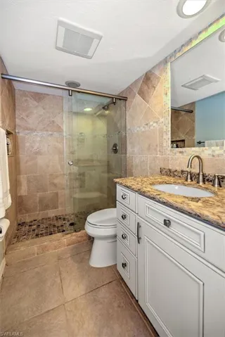 Bathroom featuring vanity, tile patterned flooring, toilet, tile walls, and an enclosed shower