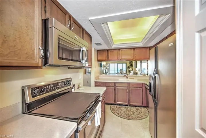 Kitchen featuring crown molding, sink, light tile patterned floors, a tray ceiling, and stainless steel appliances
