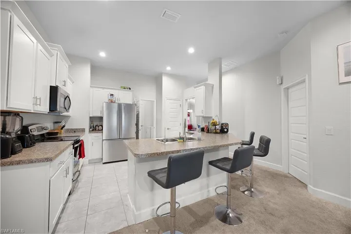 Kitchen featuring a kitchen bar, appliances with stainless steel finishes, a peninsula, white cabinets, and light tile patterned floors
