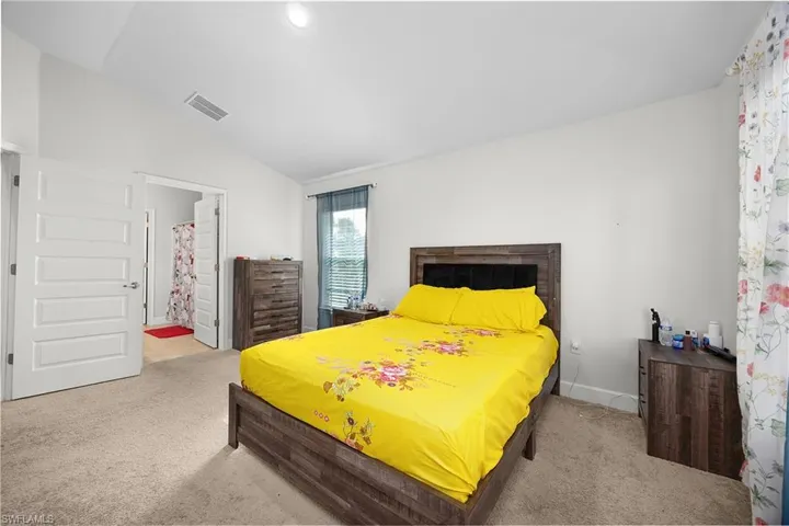 Bedroom with light carpet, vaulted ceiling, and ensuite bathroom