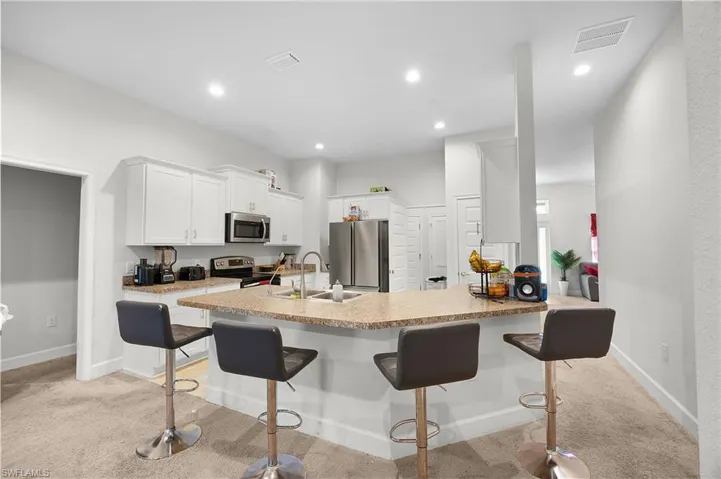 Kitchen with light carpet, a kitchen breakfast bar, appliances with stainless steel finishes, white cabinetry, and recessed lighting
