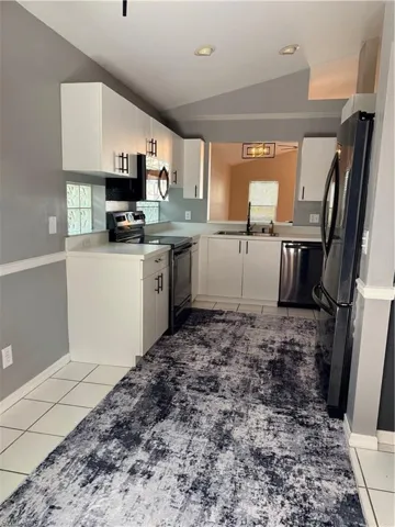 Kitchen featuring white cabinets, vaulted ceiling, range, tile floors, and fridge ample space for dining table
