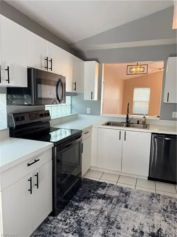 Kitchen featuring stove, white cabinetry, light countertops, black dishwasher, and vaulted ceiling