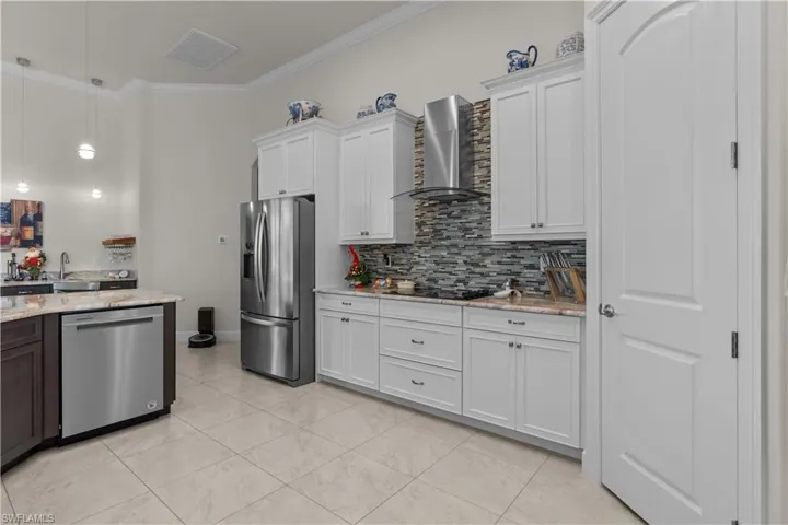 Kitchen with white cabinets, light stone countertops, wall chimney exhaust hood, and stainless steel appliances